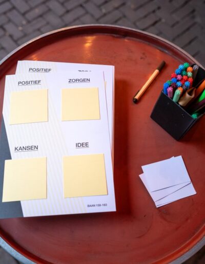 Tafel met post-its, pennen en formulieren voor het verzamelen van input van buurtbewoners over het ontwerp van Baan 159–163 tijdens een participatie-evenement.