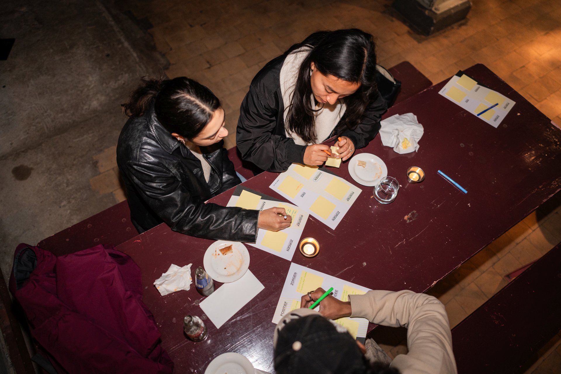 Drie buurtbewoners zitten aan tafel en vullen post-it kaarten in met ideeën, zorgen en suggesties over de toekomst van Baan 159-163 in Rotterdam.