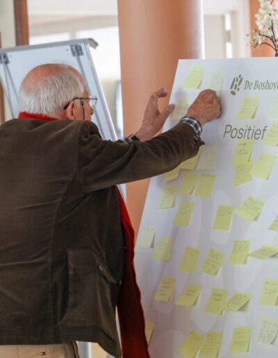 Oudere bewoner plaatst gele post-its op participatiebord tijdens MeeDenkDag voor woonproject De Boshove in Driebergen.