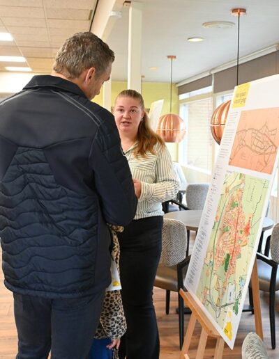 Twee volwassenen pratend bij een informatief displaybord met kaarten en tekst, tijdens de MeeDenkDag