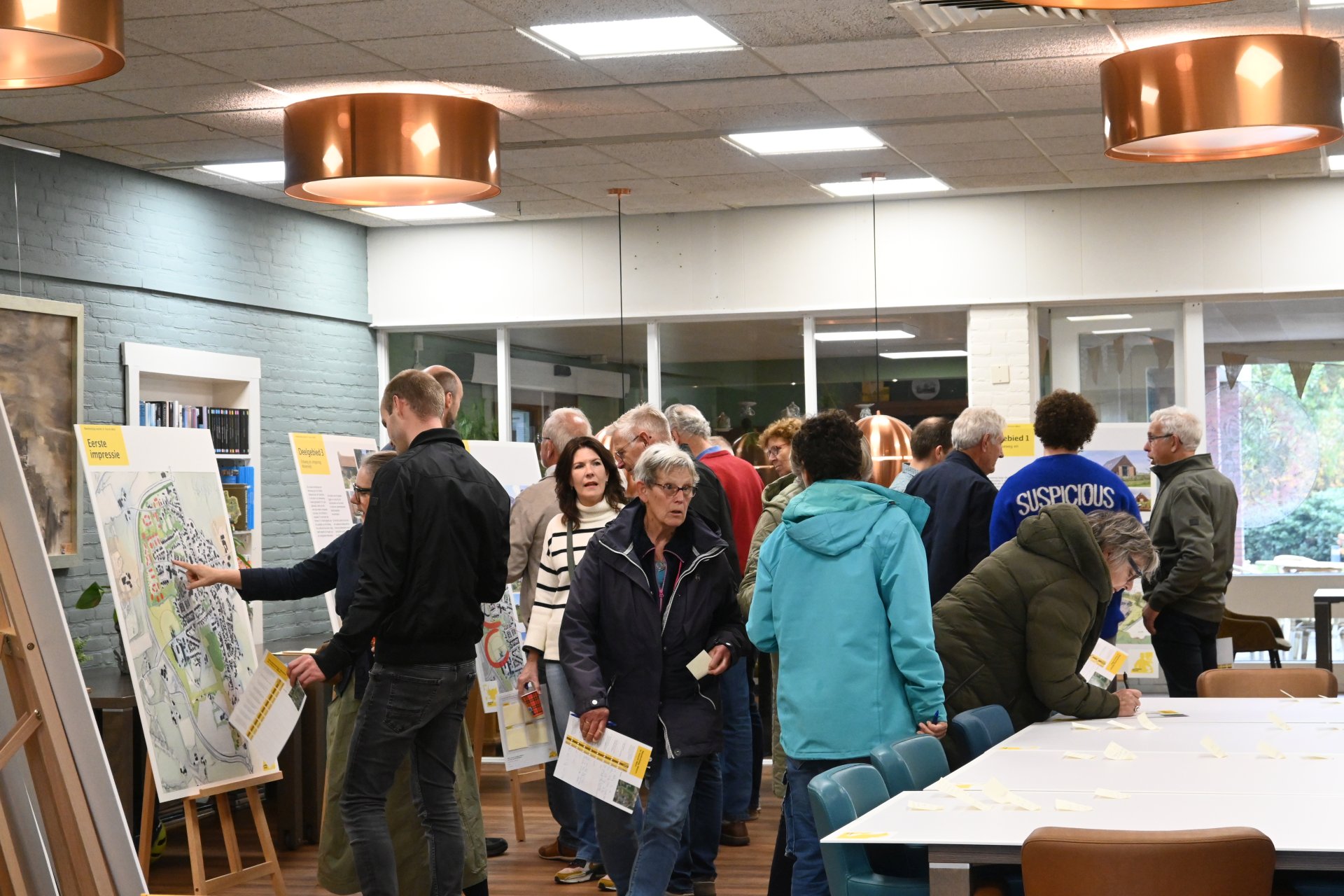 Groep mensen in een moderne ruimte die posters en kaarten bekijken tijdens de MeeDenkDag over stadsplanning in Voorst