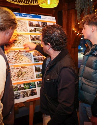 Drie bezoekers bekijken een overzichtsbord met kaarten, diagrammen en foto's onder de titel 